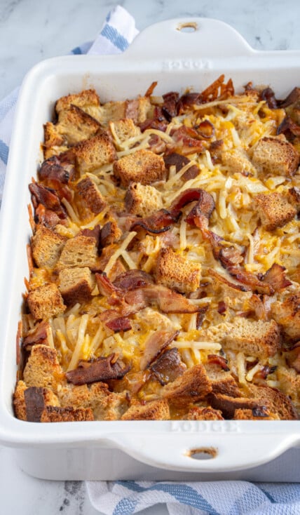 White dish holding baked breakfast casserole with hash browns, bacon, and bread including cheddar cheese.