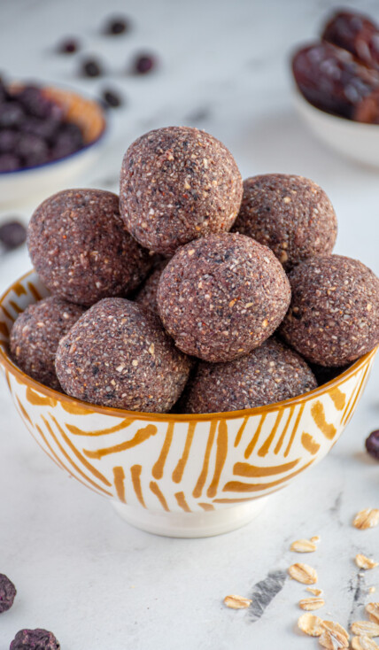Bowl of purple colored blueberry energy balls surrounded by freeze dried blueberries.